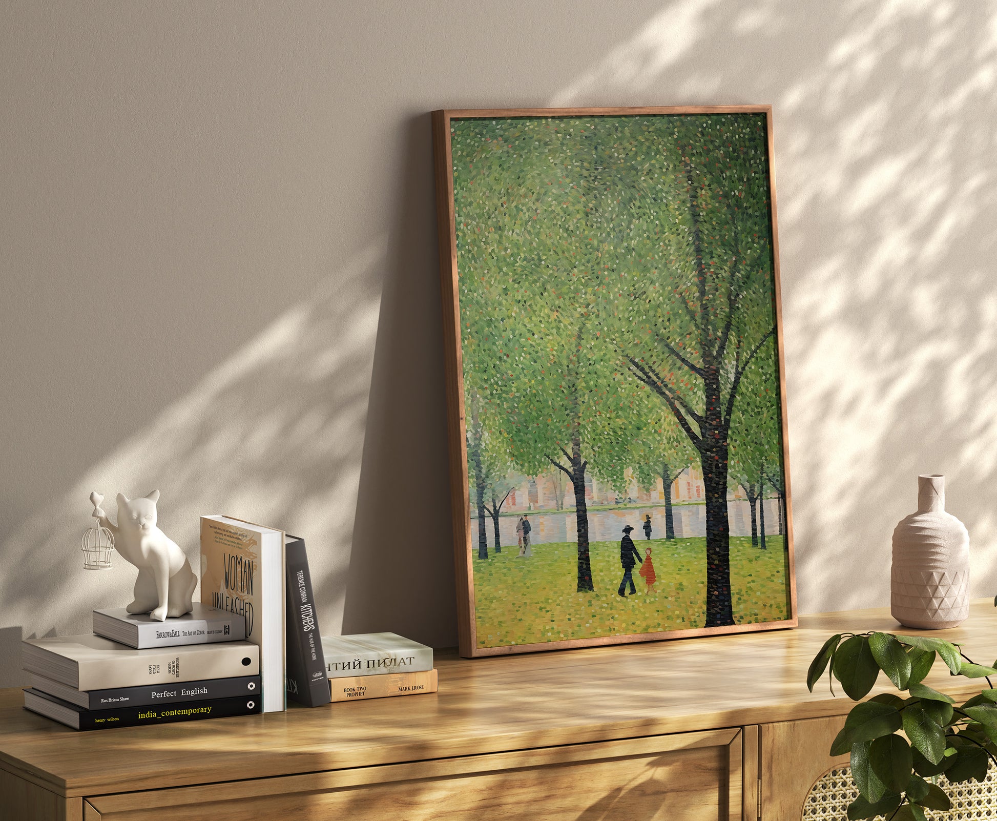 A framed painting of a park scene placed on a floor leaning against a wall, with books and decor items nearby.