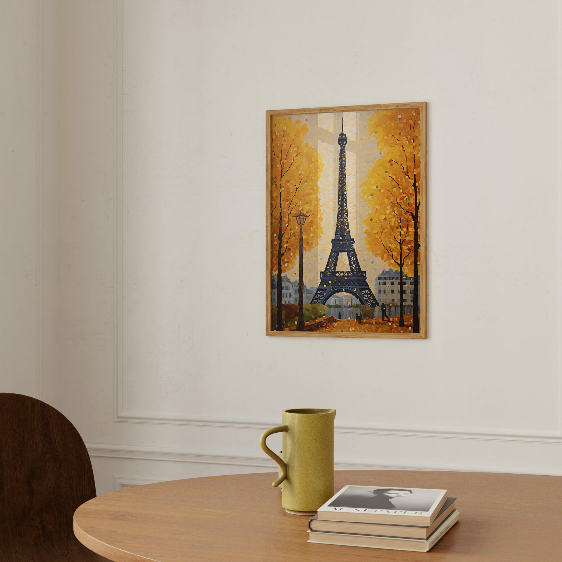 A painting of the Eiffel Tower amidst autumn trees, displayed above a table with a mug and books.