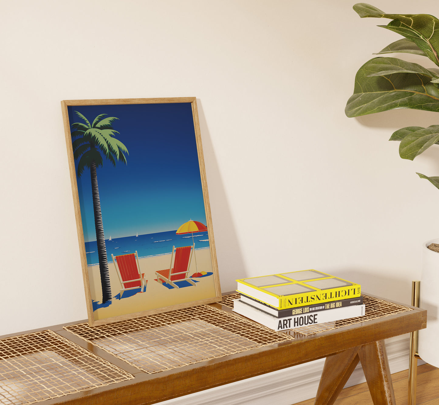 A tropical beach poster leaning against a wall on a side table with decorative books.