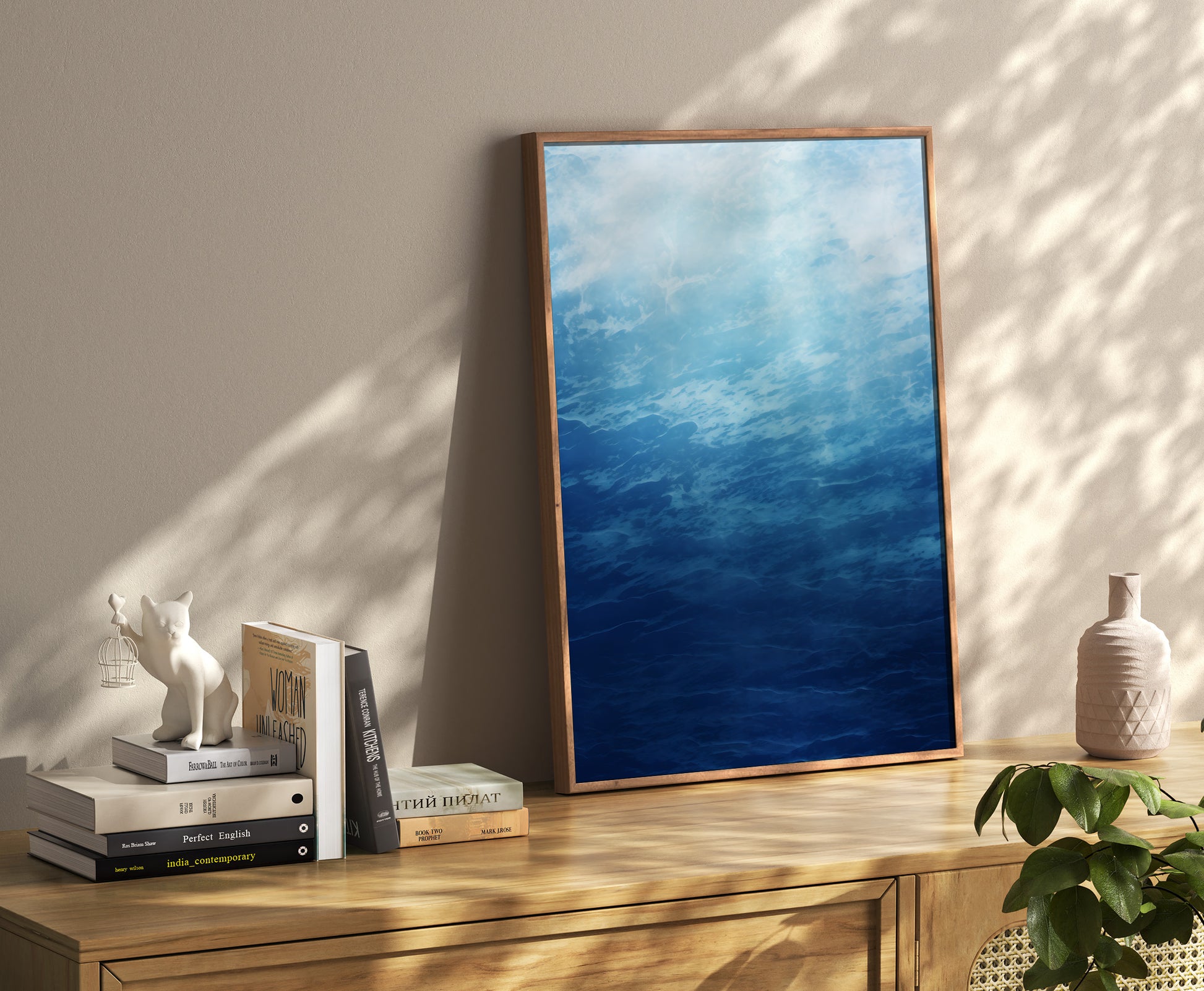 A framed painting of a blue sky leaning against a wall beside books and decor.
