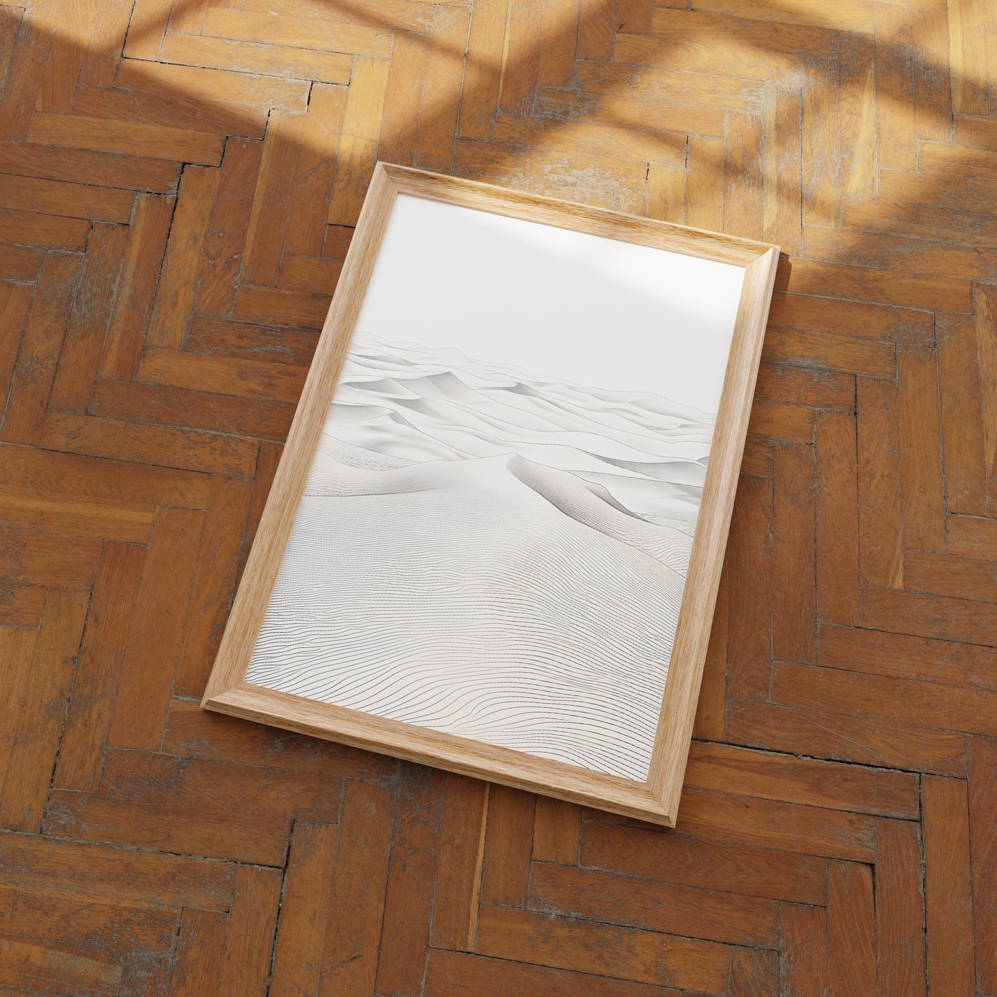 A framed picture of sand dunes lying on a herringbone pattern wood floor.