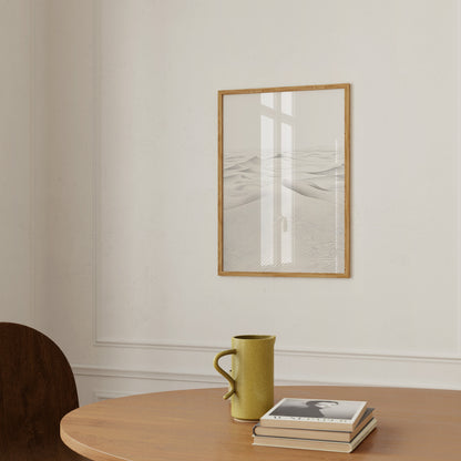 A framed desert landscape picture on a wall above a table with a mug and a book.