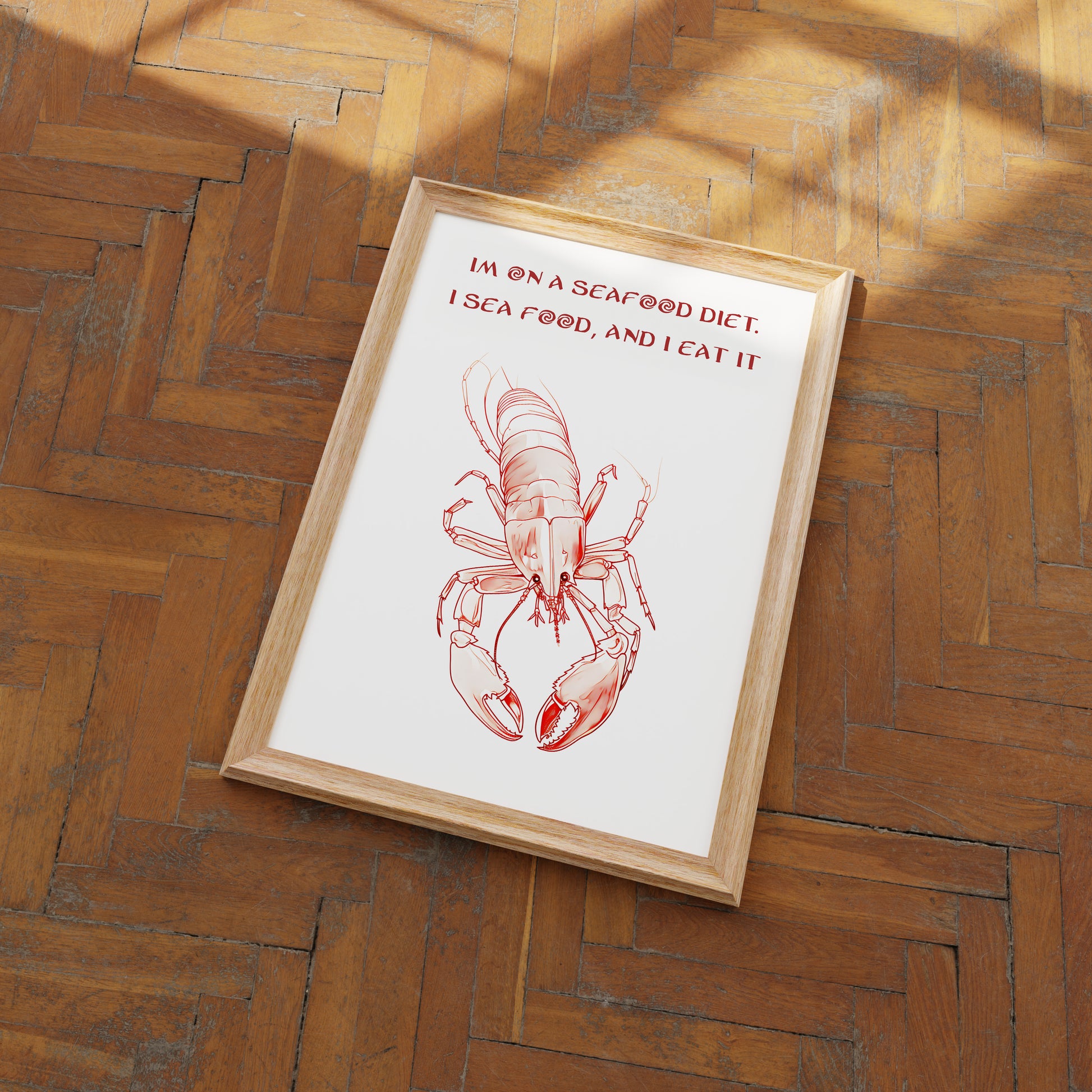 A framed picture of a lobster with a pun "I'm on a seafood diet. I see food, and I eat it" on a wooden floor.