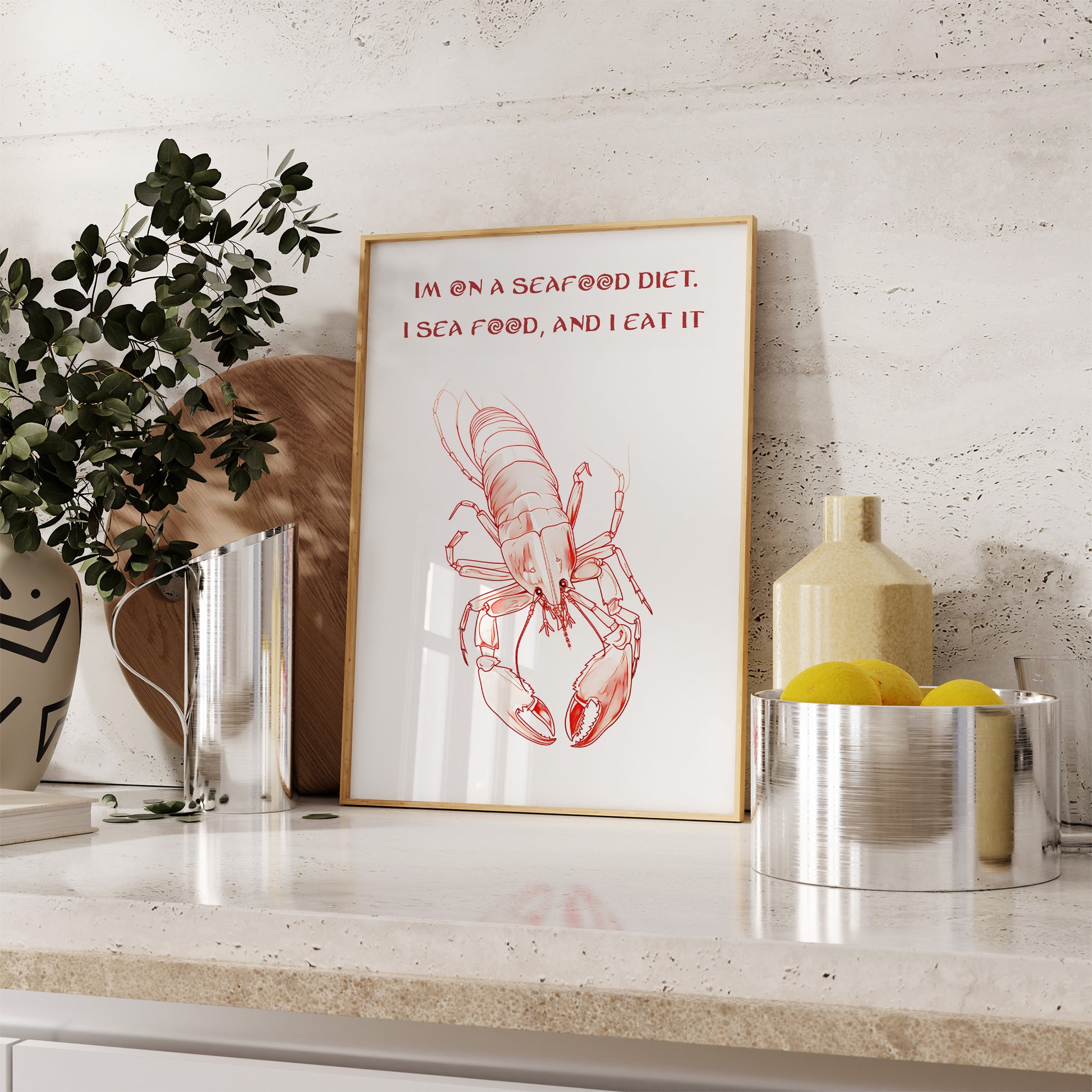 A framed image with a lobster illustration and a pun "I'm on a seafood diet. I sea food, and I eat it" on a kitchen counter.