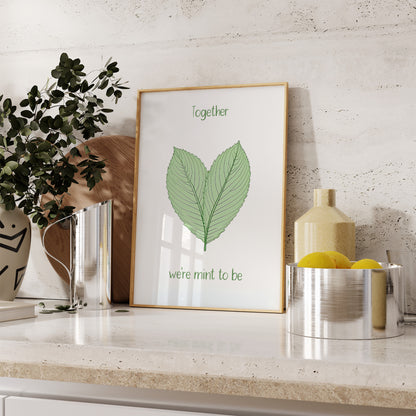 Framed artwork with leaf illustration and pun "together we're mint to be" on a kitchen counter.