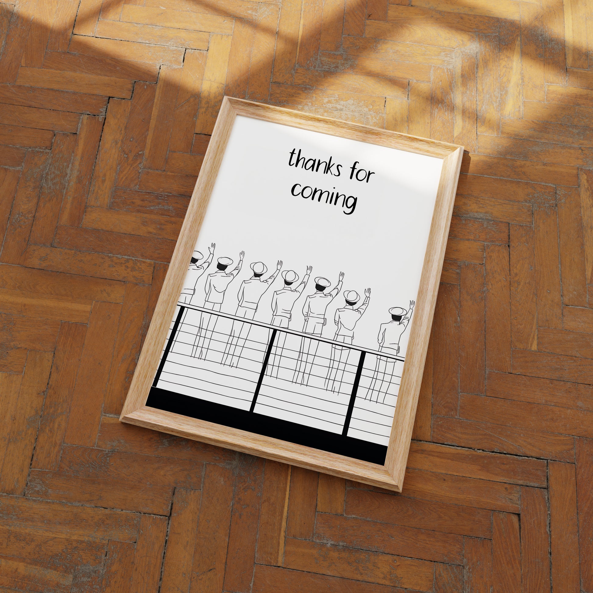 A framed picture on a wooden floor with a drawing of people waving goodbye and the text "thanks for coming."