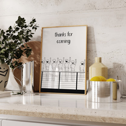 A framed poster with a "thanks for coming" message displayed in a stylish kitchen setting.