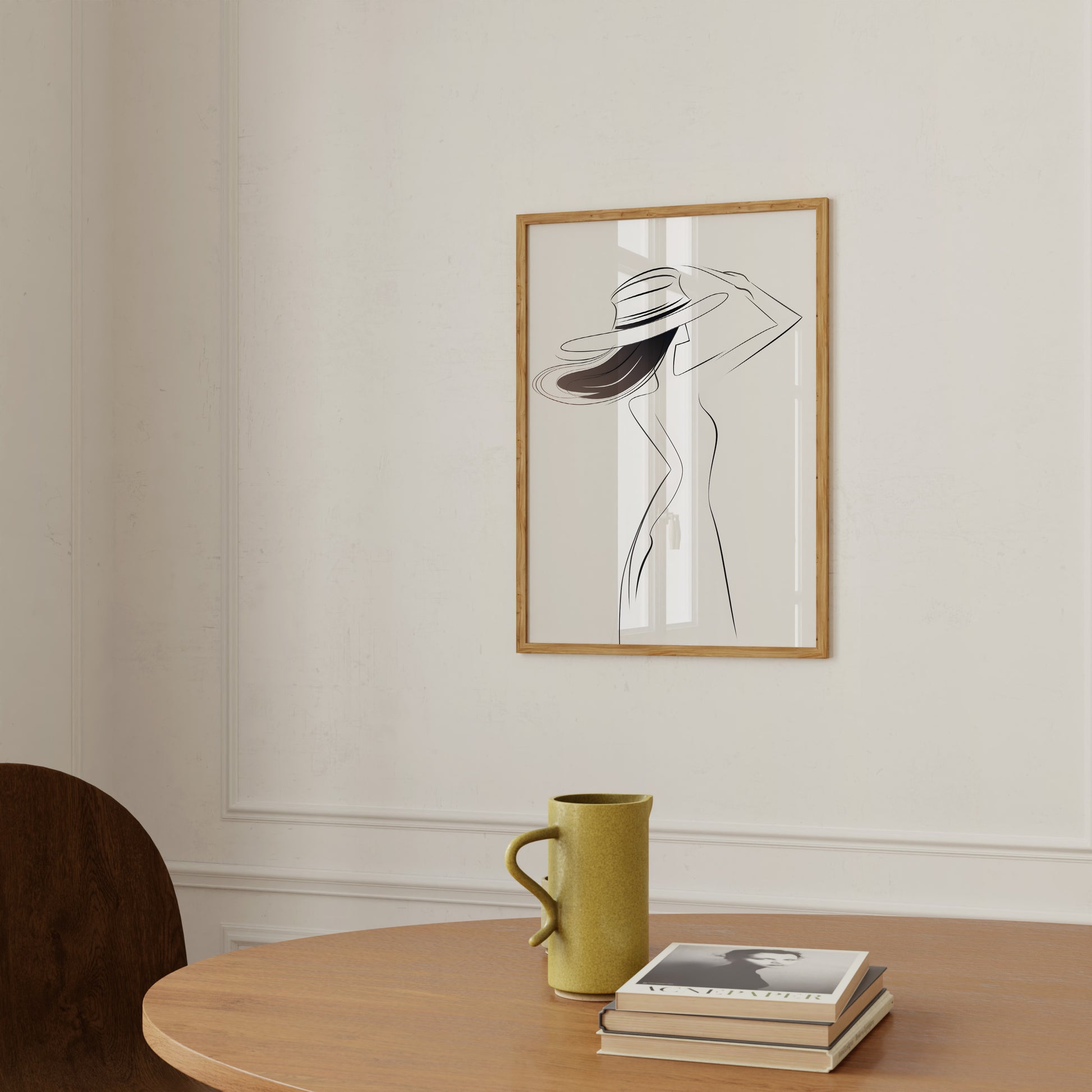Minimalist artwork of a woman in a frame on a wall above a table with a mug and books.