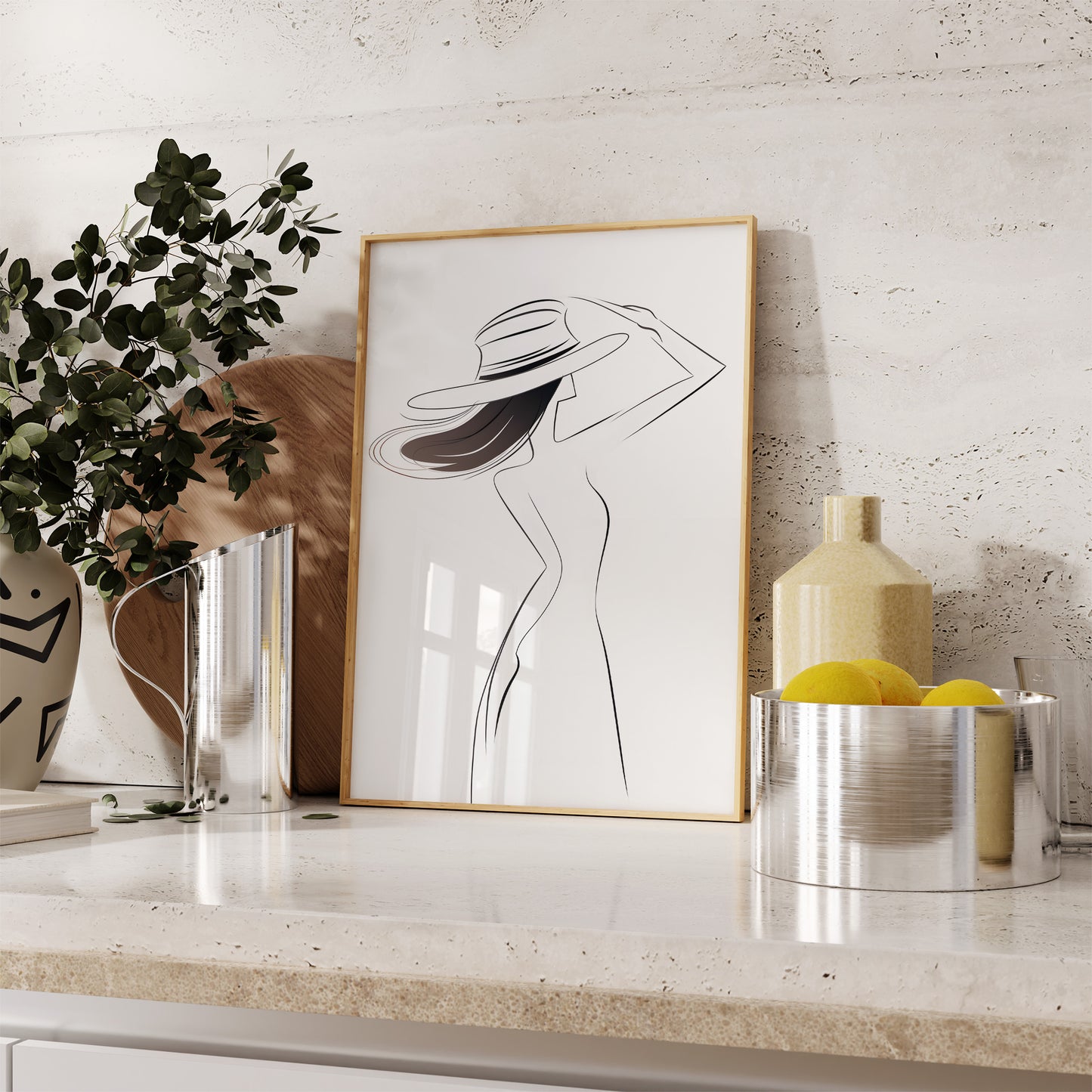 Elegant framed line art of a woman with a hat on a kitchen counter, beside a plant and lemons.