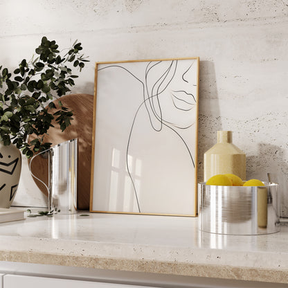 Modern line art in a gold frame on a kitchen countertop with decorative items.